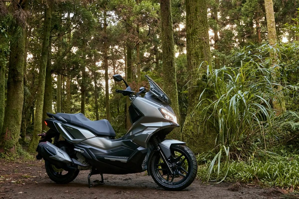 Un scooter SYM ADX posé dans une forêt
